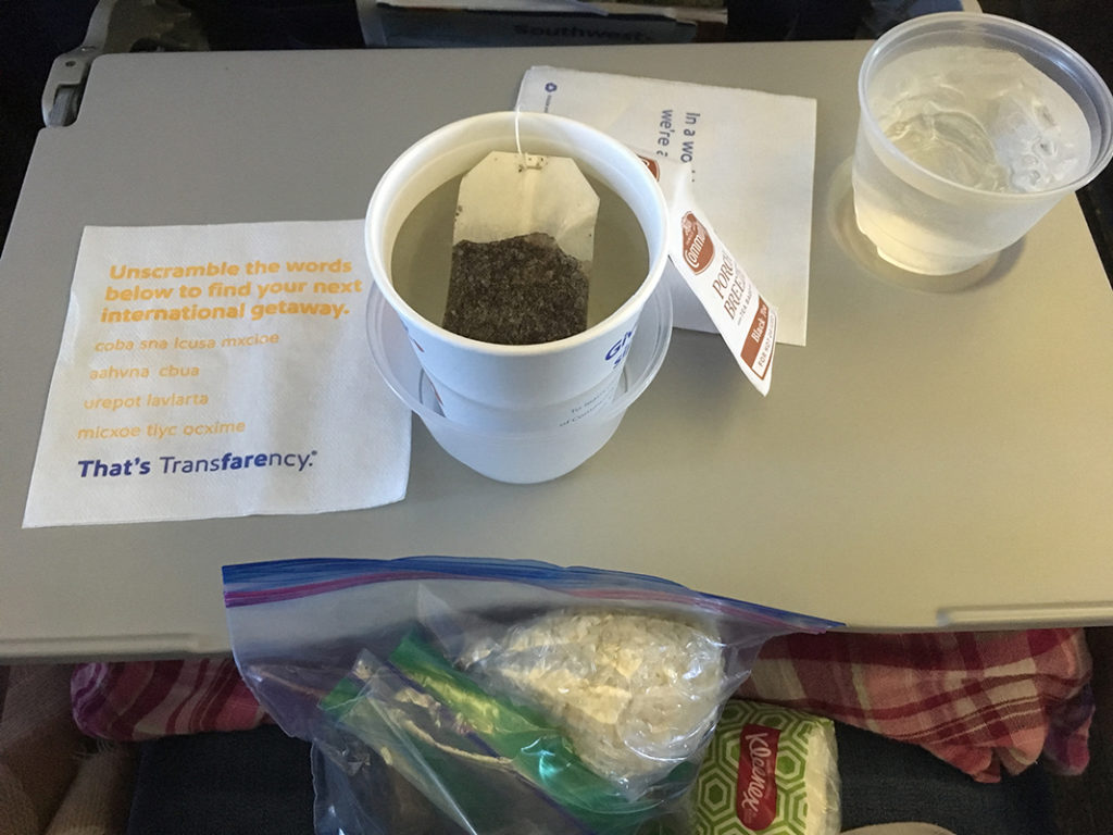 Image of my hot tea and water on Southwest Airlines, next to the snacks I brought from home